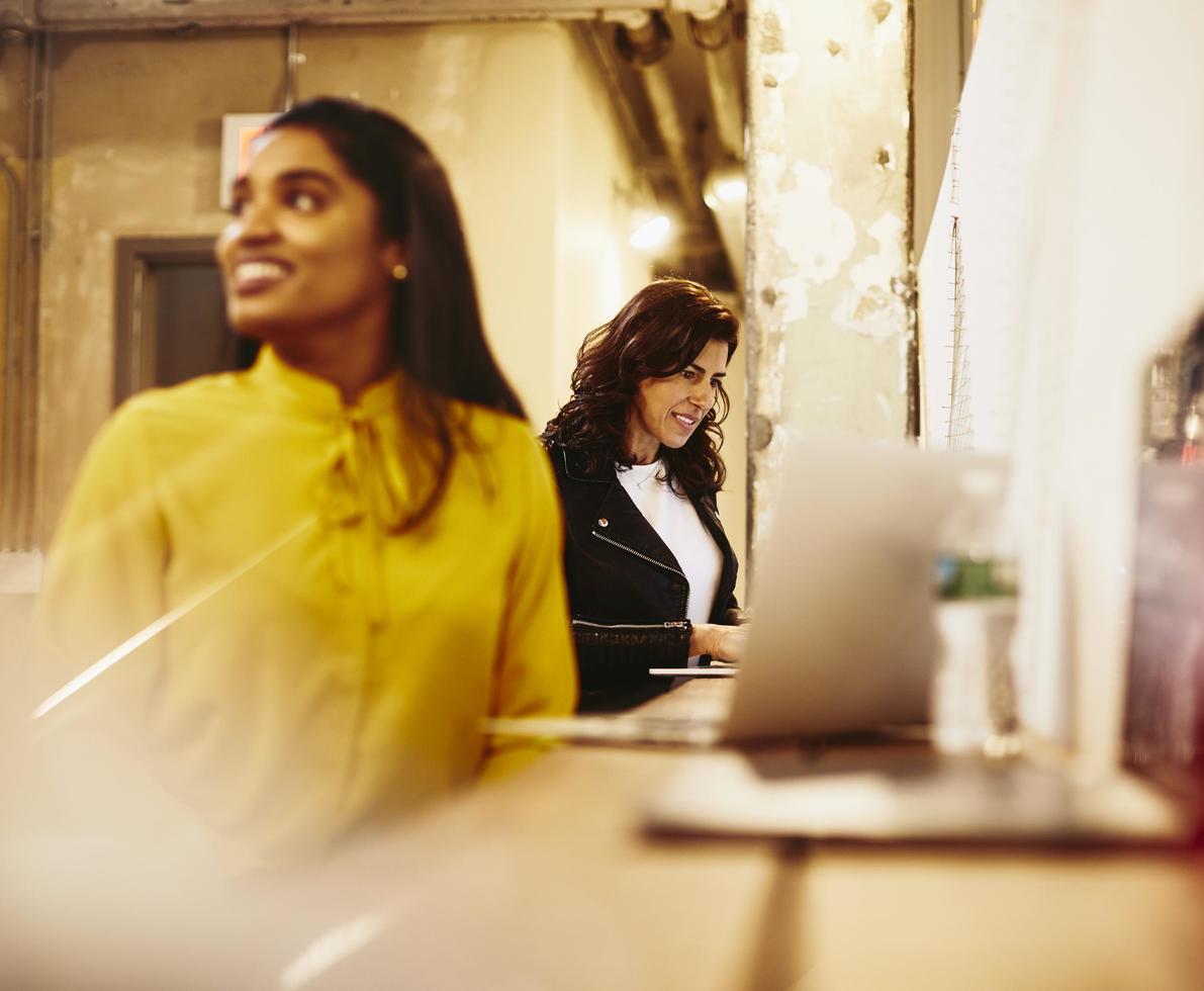 Two smiling women working on their laptop.